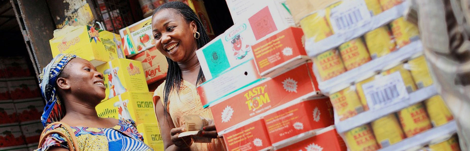 Customer buying packaged foods from a shop owner at her stall, Nigeria, Olam. 